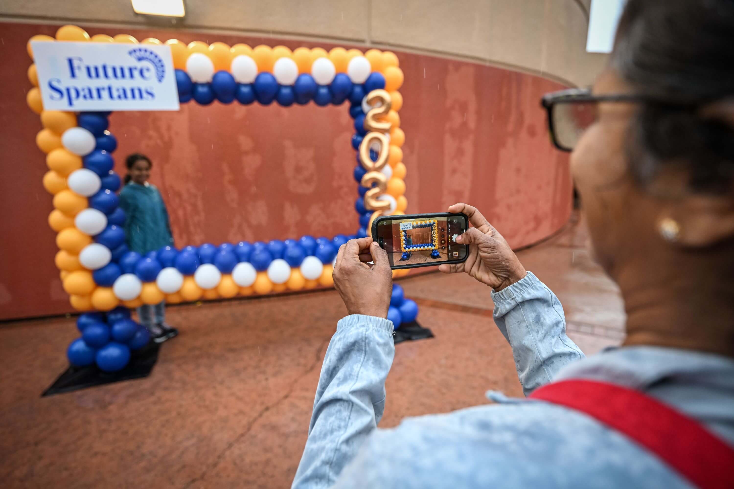 a mother takes a photo of her daughter in front of a future spartans sign