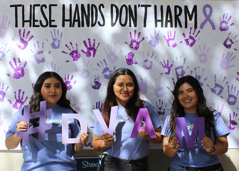 three college students beneath a sign that reads these hands don't harm