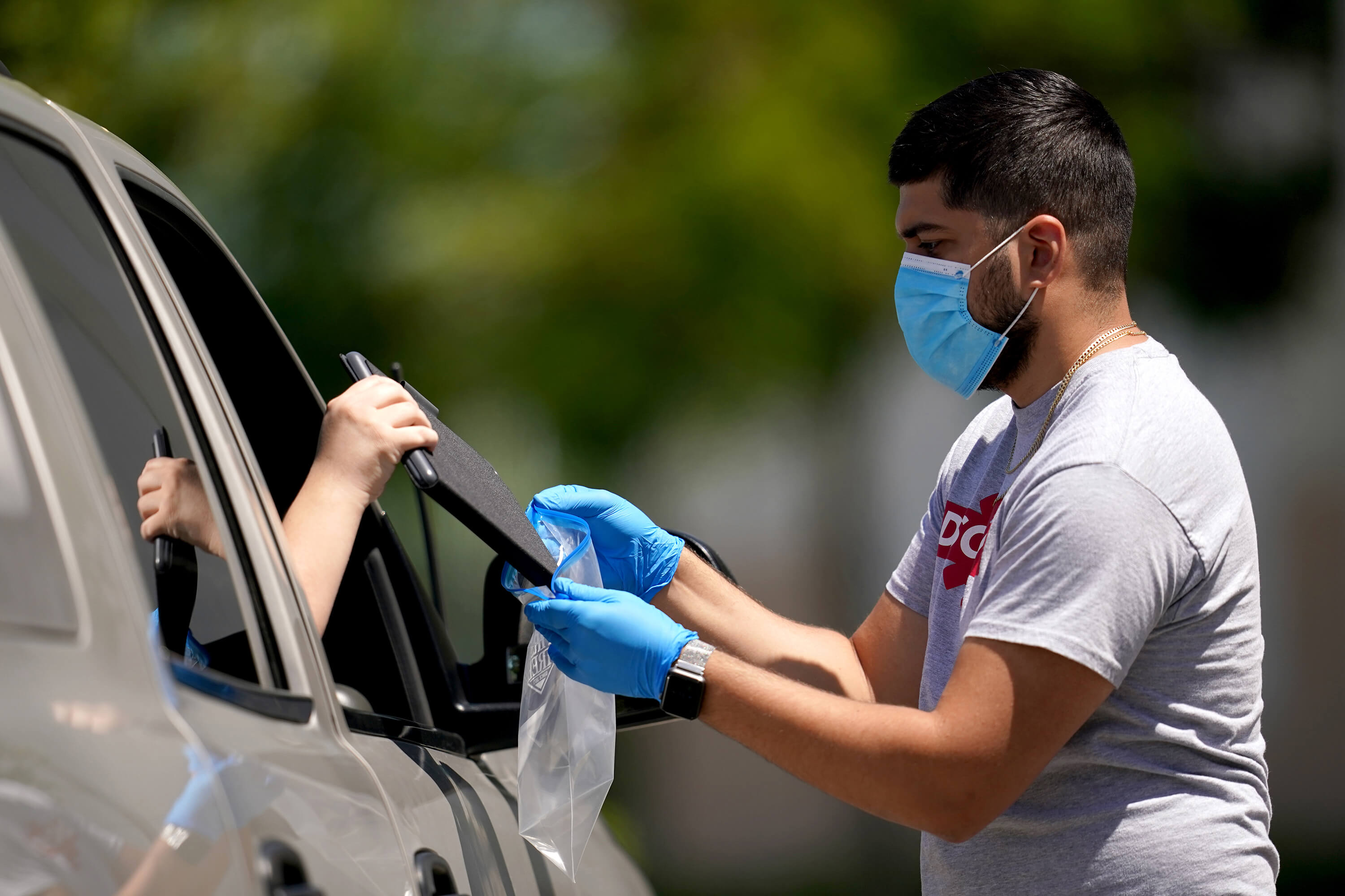 A man wearing a face mask handing a tablet to a person.