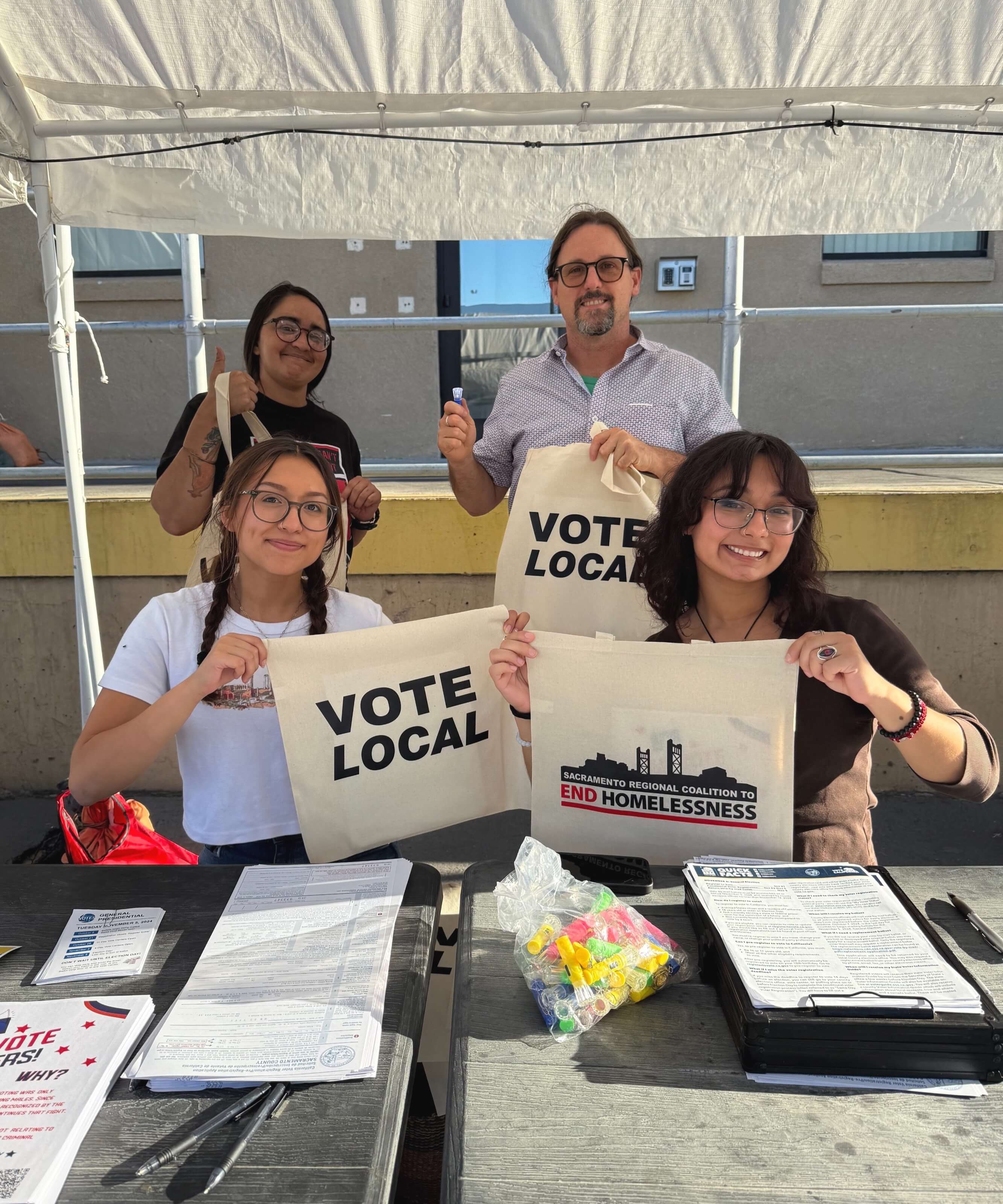 three college students and an employee holding up a sign that says vote local