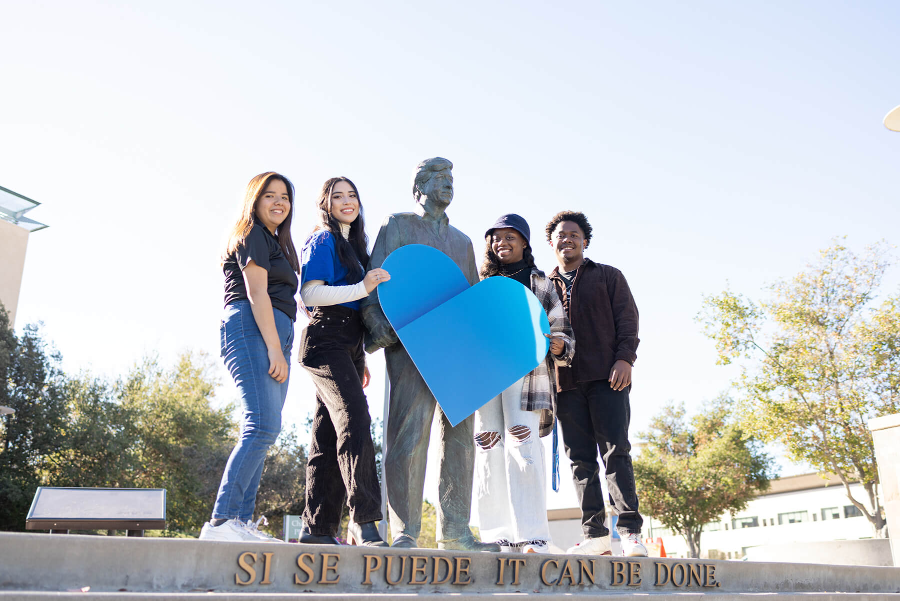 c s u san marcos students standing with a blue paper heart in front of a statue of cesar chavez