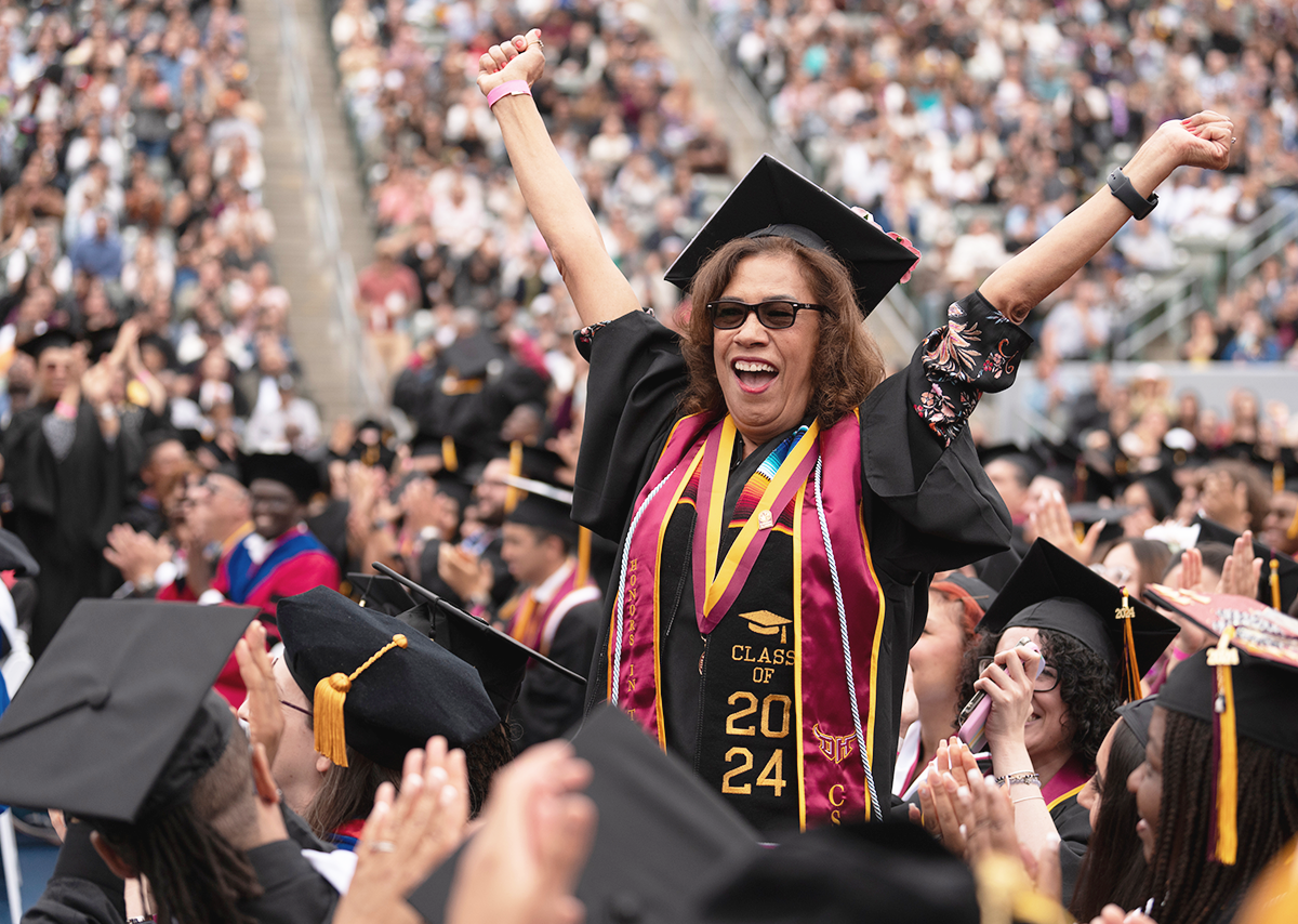 A student standing with her hands up in celebration at a 2024 CSU Dominguez Hills graduation.