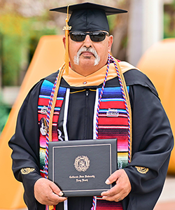 Joseph Valadez posing with sunglasses on in his CSULB cap and gown.