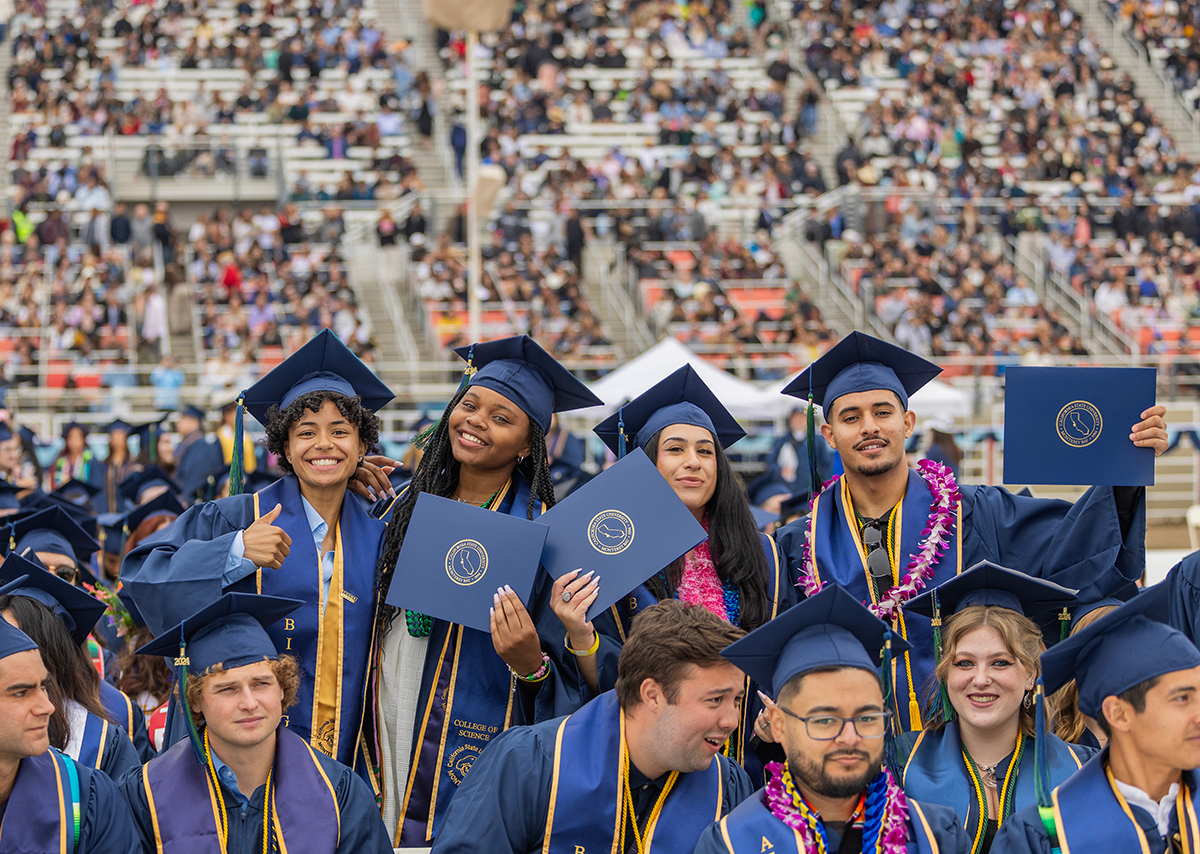 Students holding their diplomas and smiling at their graduation at Cal State Monterey Bay in 2024.