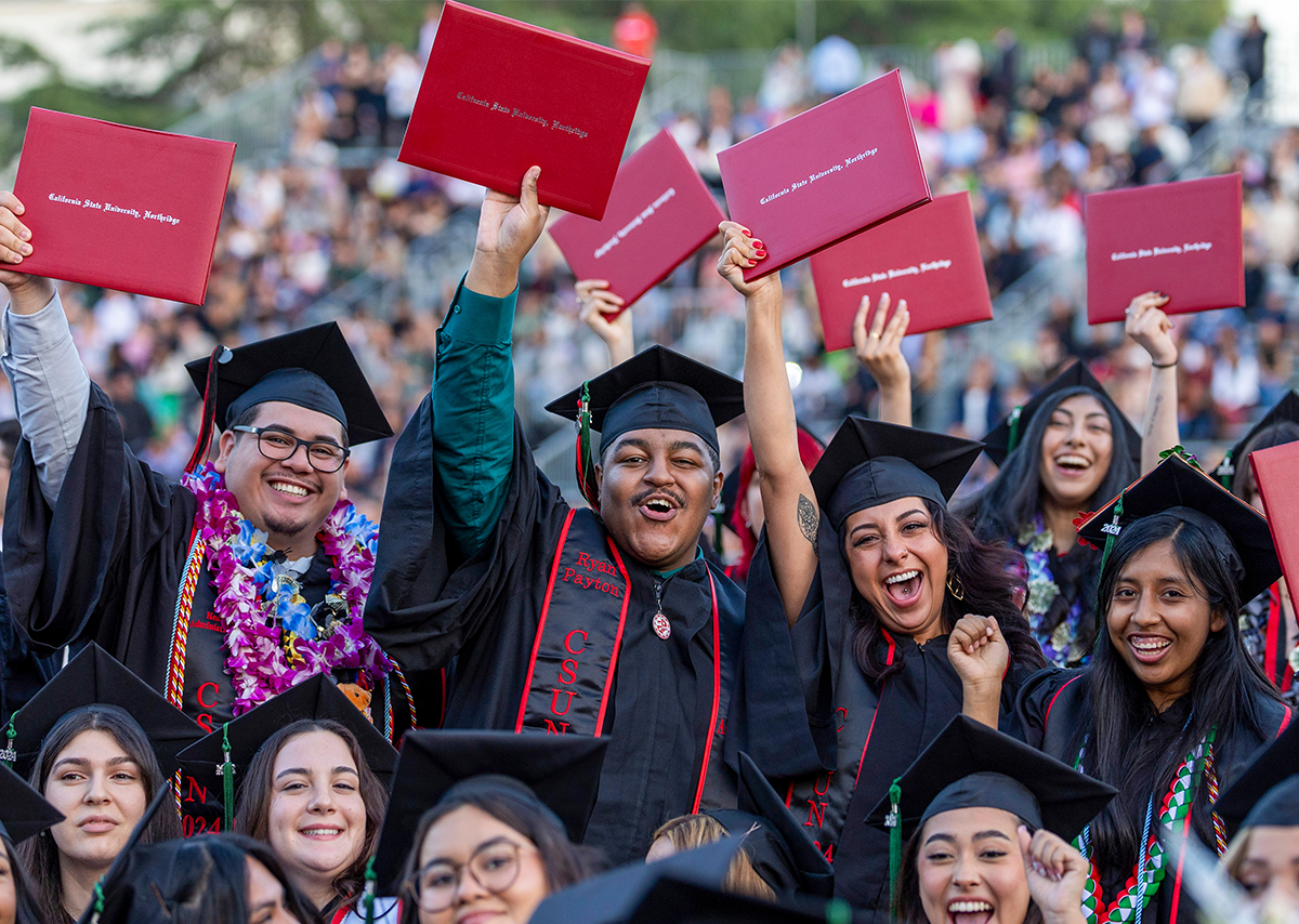 CSUN students celebrating their graduation in their cap and gowns holding up their diplomas.