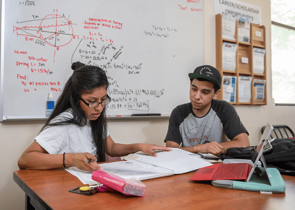 A Latinx female and male student working on an assignment in a classroom.