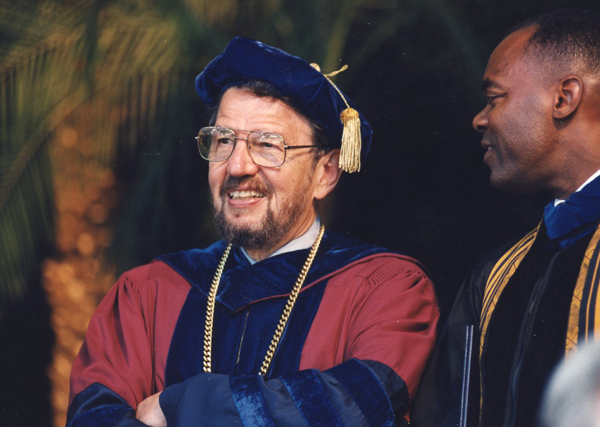 Former San Francisco State President Robert Corrigan smiling at a commencement ceremony.
