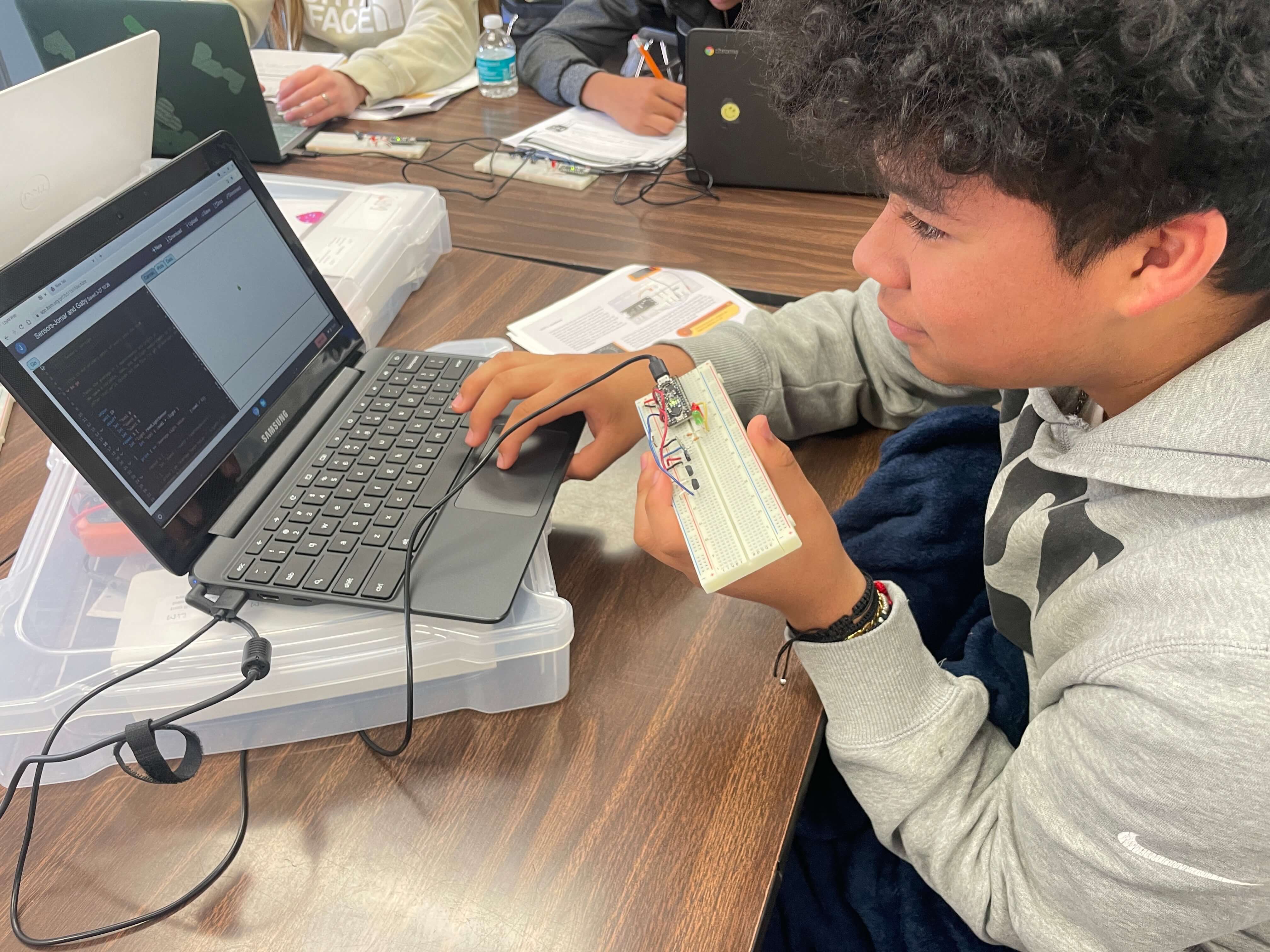 High school student holds BasicBoard and looks at measurement on laptop